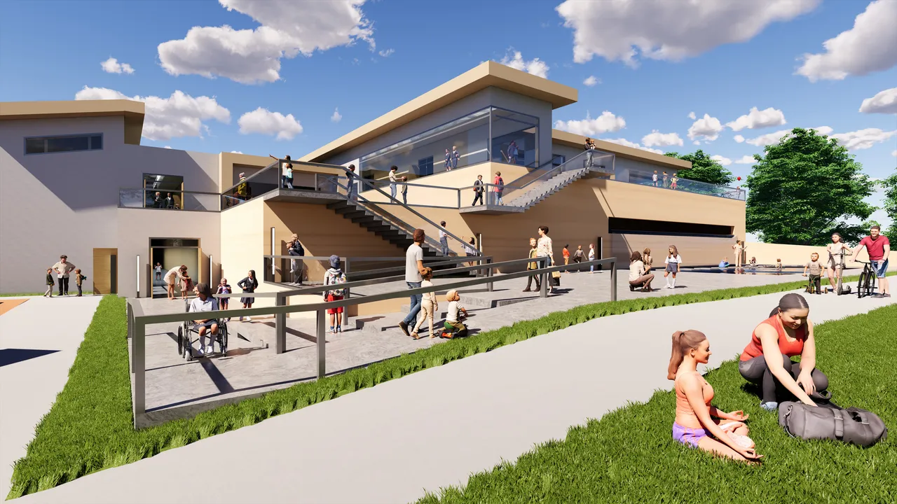 The same school from the playing field. An open external stair climbs the sand-coloured facade to a glazed upper storey, with ramps and guardrails threading the terrace below and children spread across the paving and grass.